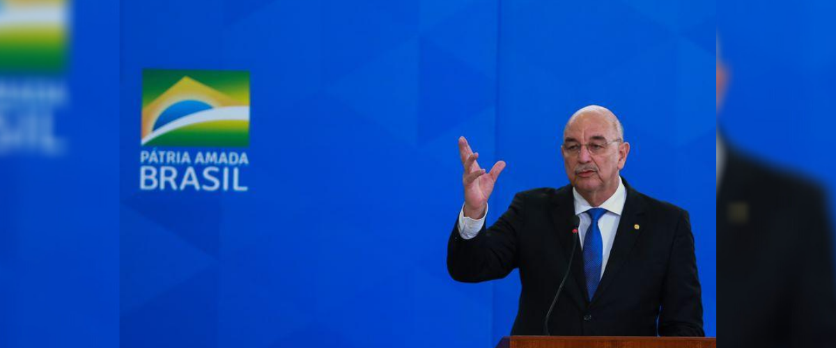 Osmar terra aparece em frente à painel com slogan do governo bolsonaro.