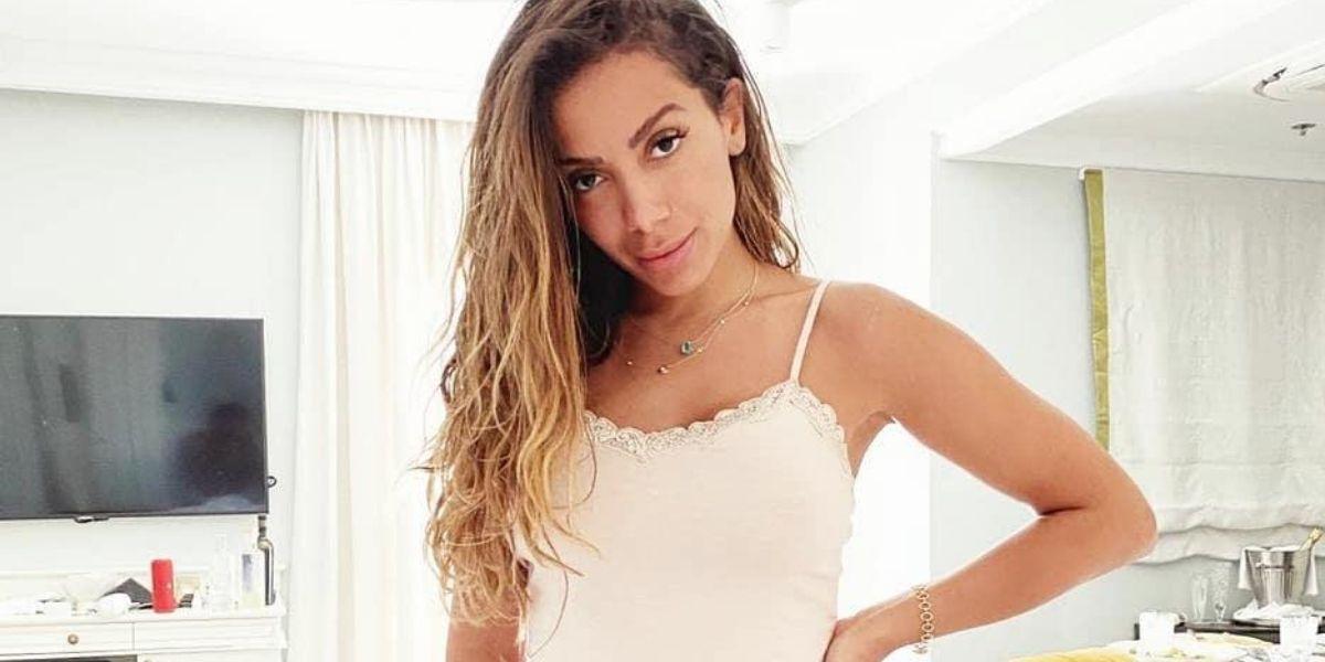 Anitta posada olhando para frente em cima da cama usando lingerie clara