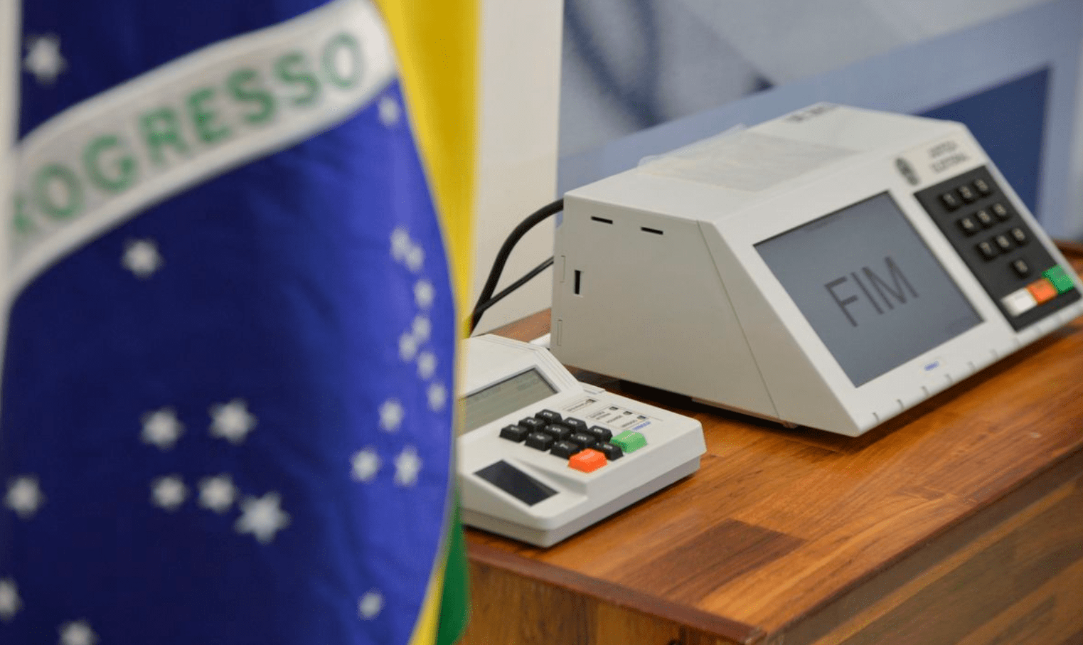 Foto mostra urna eletrônica e uma bandeira do brasil