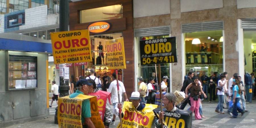 Pessoas segurando placa de compro ouro em rua comercial