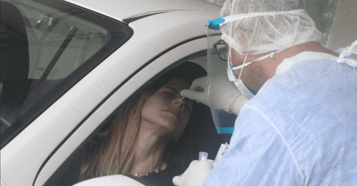 Foto mostra profissional coletando exame pcr de paciente dentro do carro.