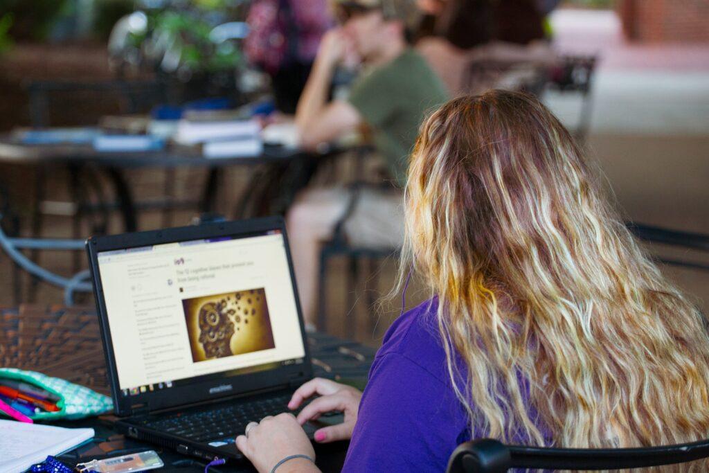 Mulher de costas, sentada em frente a um notebook digitando