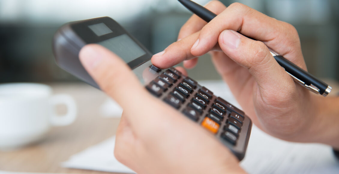 Imagem aproximada mostra mão masculina segurando e digitando em calculadora