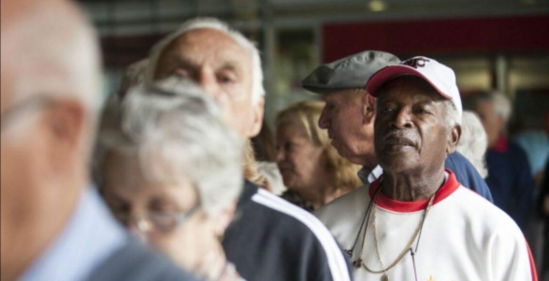 Foto mostra fila com pessoas idosas e aposentados.