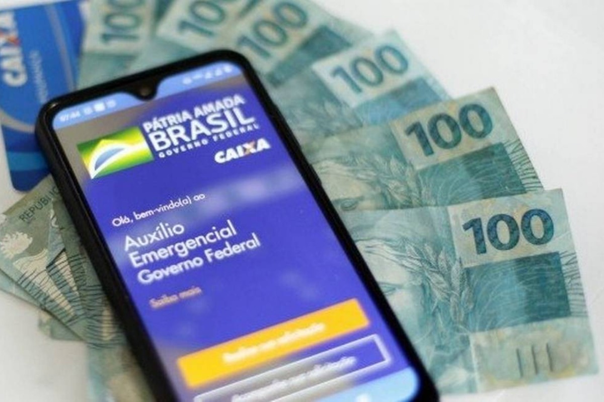 Imagem mostra celular com o aplicativo do novo auxílio emergencial e notas de cem reais