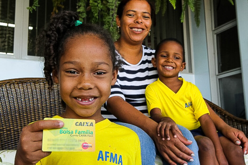 Uma família sorridente exibe o seu cartão do Bolsa Família